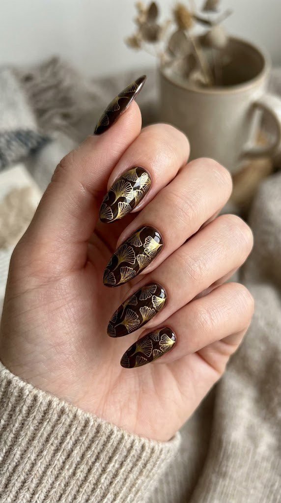Long almond nails with liquid gold ginkgo leaf illustration on dark chocolate brown gel