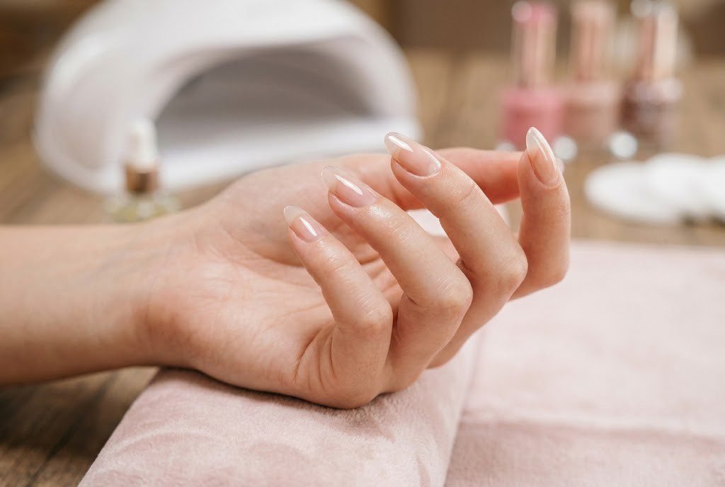 Close up of natural looking gel manicure with clear sheer gel polish on almond nails resting near UV lamp