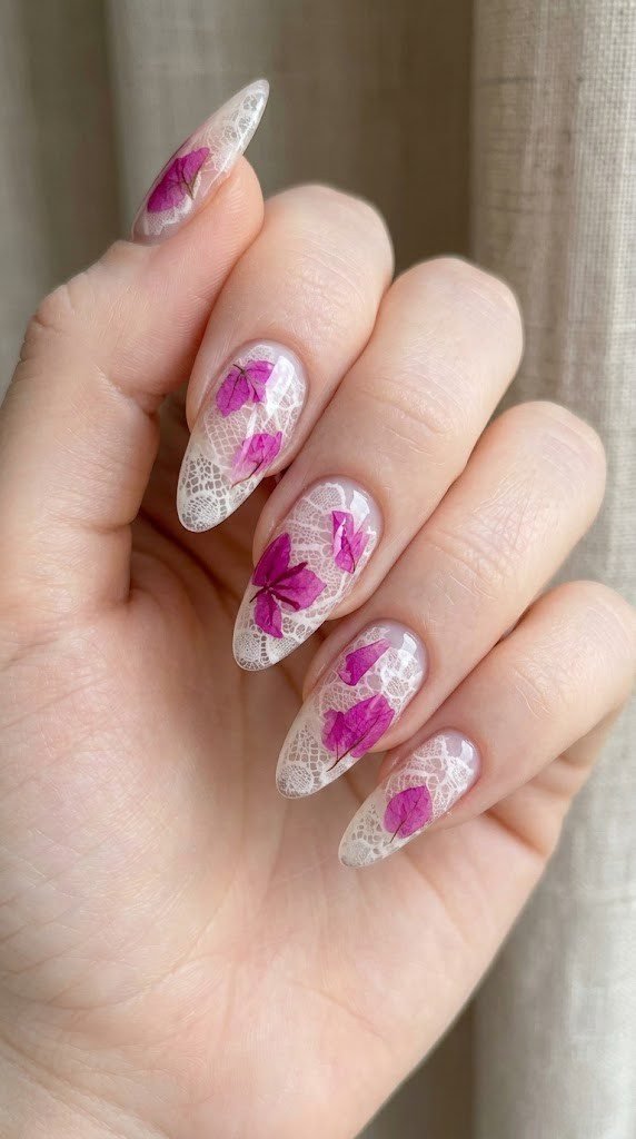 Clear gel almond nails with white lace fishnet pattern and vivid magenta bougainvillea petals