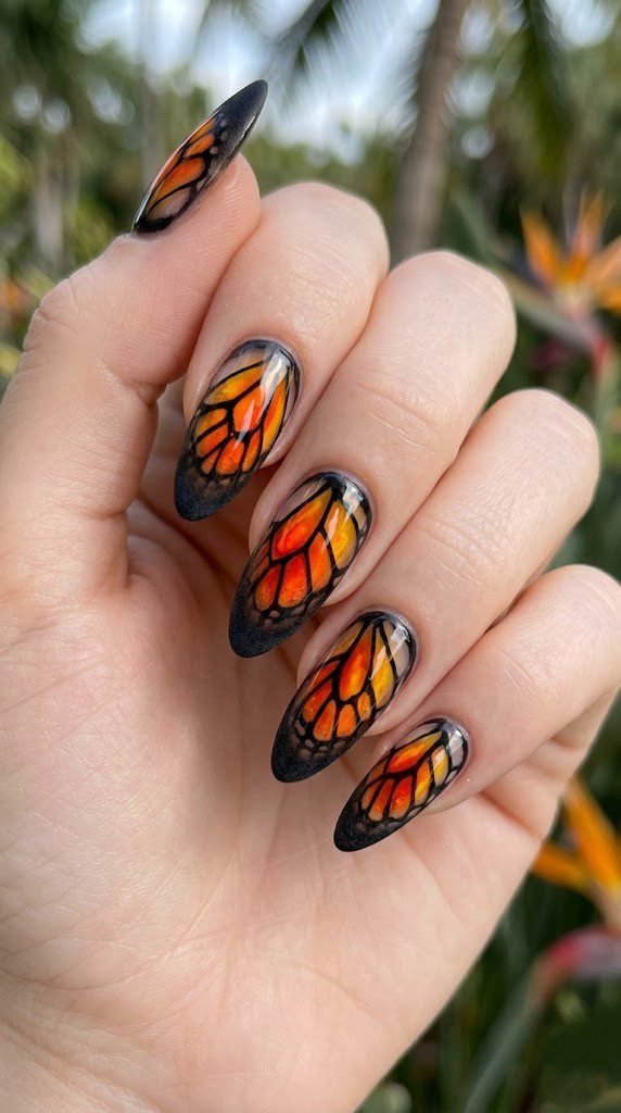 Almond nails designed as monarch butterfly wings with fiery orange gradient and black linework tips
