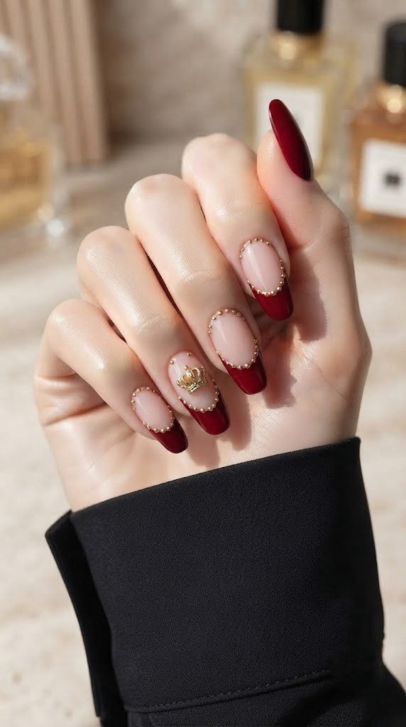 Glossy red French tip nails with a tiny sculpted gold crown charm