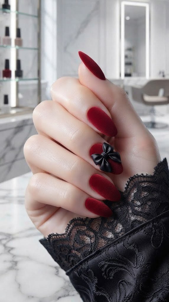 Red velvet textured nails with a sculpted black satin bow appliqué accent