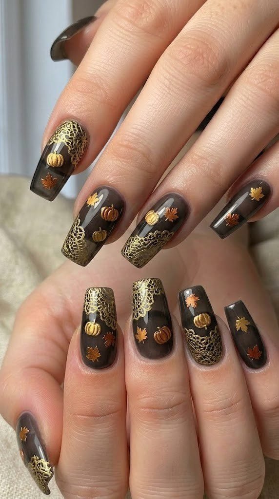 Sheer black nail design with 24k gold lace detailing and tiny pumpkin charms for autumn