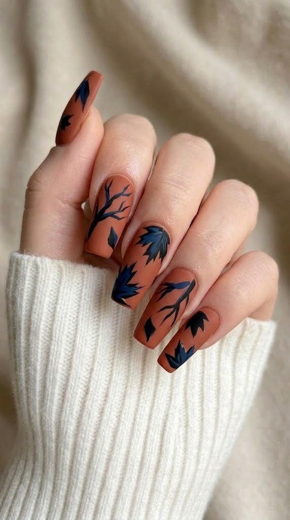 Matte terracotta nails with bold navy and black autumn branch and leaf artwork